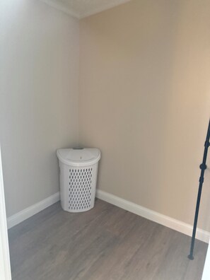 A corner of a room with a white trash bin against a beige wall and a grey floor.