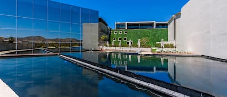 Un espace piscine moderne avec une eau d’un bleu limpide, un bâtiment en verre et un mur végétal.