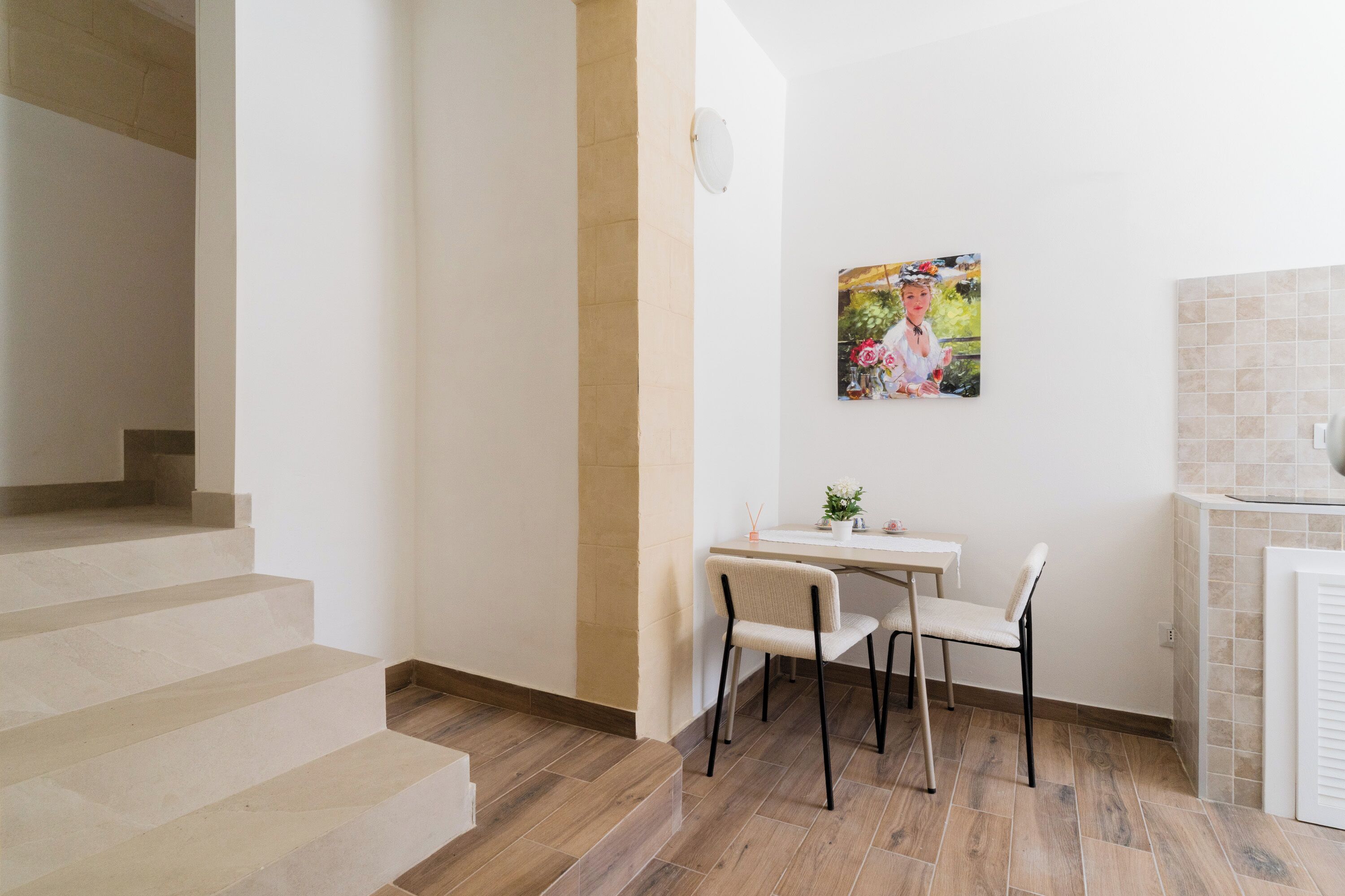 A staircase leading to a room with a dining area, a painting on the wall, and a tiled backsplash.
