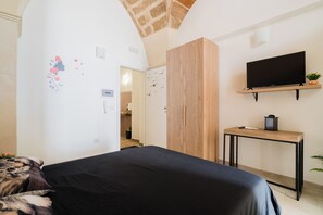 A bedroom with a bed, a TV mounted on the wall, a wooden wardrobe, and a small table with a plant. - Maxmar - Mono Classic by BarbarHouse (Lizzanello)