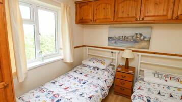 A bedroom with two single beds, wooden cabinets, a window with curtains, a bedside lamp, and a painting on the wall.