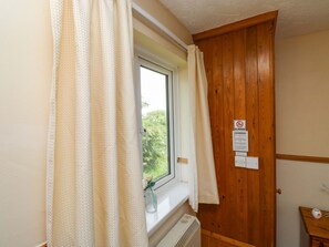 Ein Zimmer mit Fenster, Holztür, Heizkörper und einem kleinen Tisch mit Zahnbürste und Flasche.