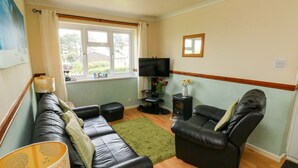 A living room with a sofa, two armchairs, a TV, a fireplace, and a window with curtains. - Seascape Retreat (Brixham)