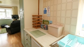 A kitchen with wooden shelves, a trash bin, a sink with dishes, and a television in the corner. - Seascape Retreat (Brixham)