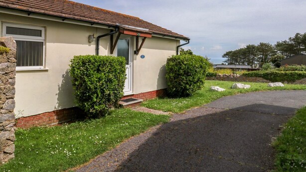 A single-story house with a tiled roof, a front door, and a small front yard with a paved driveway. - Seascape Retreat (Brixham)