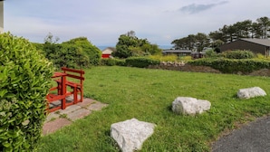 A grassy area with a red bench, a stone pathway, and a view of houses and trees. - Seascape Retreat (Brixham)
