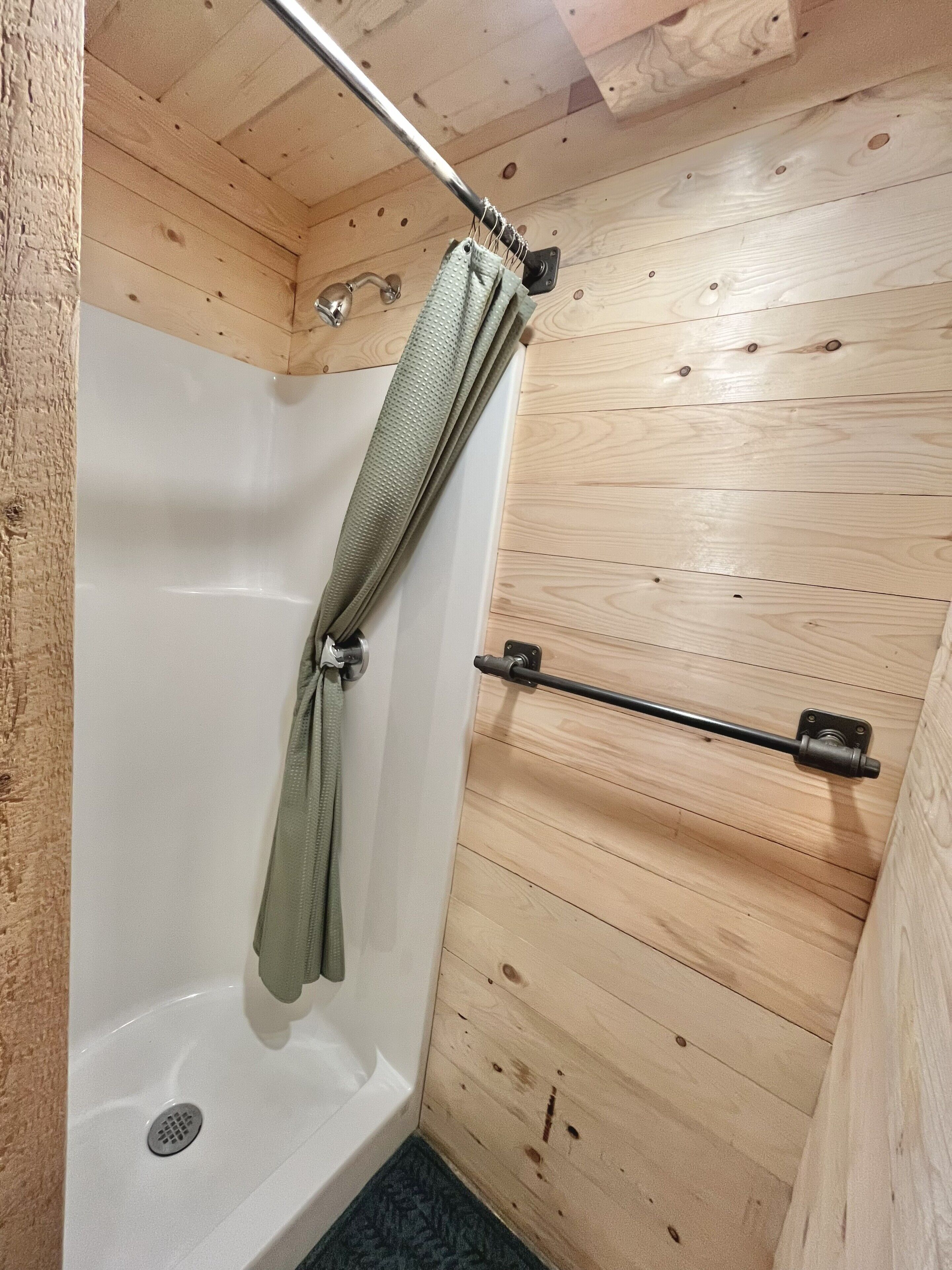 Een badkamer met houten lambrisering, een douche, een handdoekrek en een metalen handgreep.
