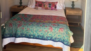 A bedroom with a wooden ceiling, a ceiling fan, a bed with a colorful quilt, two bedside lamps, and a green abstract painting on the wall. - Awesome 3-bedroom house with AC in charming Burnsville (Burnsville)