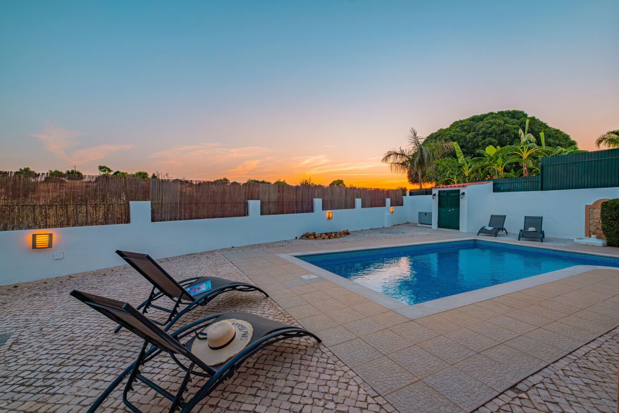 A swimming pool with lounge chairs and a sunset view.