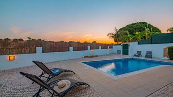 A swimming pool with lounge chairs and a sunset view.