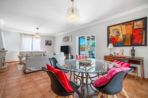 A modern living room with a glass dining table, black chairs, a sofa, and a TV.