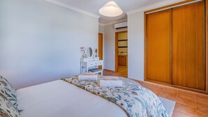 A bedroom with a bed, a bedside table with a mirror, a hanging light fixture, and a wardrobe.