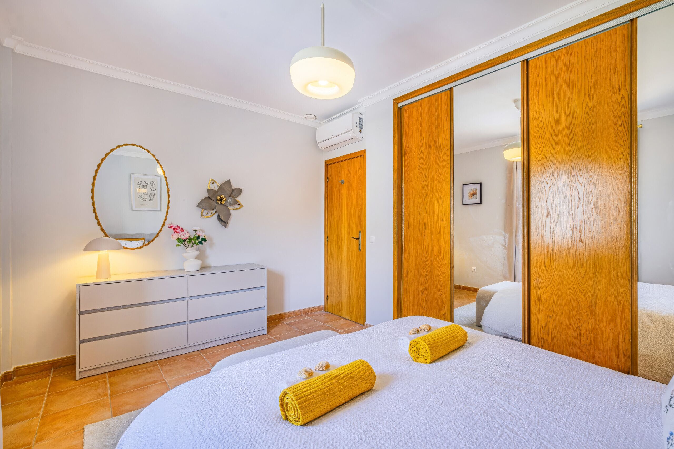 Una camera da letto con un letto, una cassettiera, uno specchio, un condizionatore d'aria a parete e un armadio in legno.