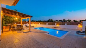 A swimming pool with a pergola and seating area, surrounded by a fence and trees.