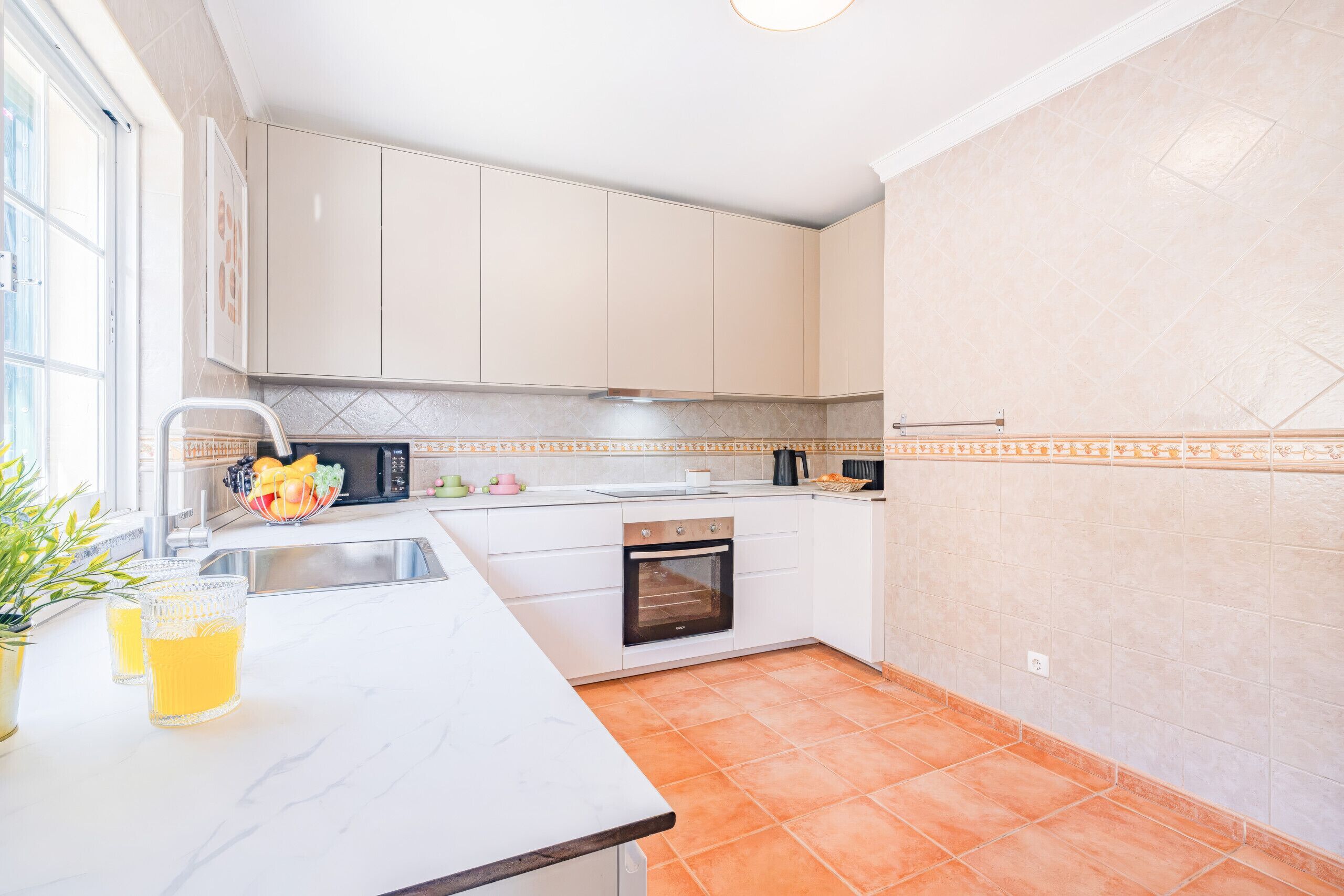 Una cocina con armarios blancos, un lavamanos de acero inoxidable, un microondas y un salpicadero de azulejos.