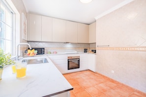 A kitchen with white cabinets, a stainless steel sink, a microwave, and a tiled backsplash.