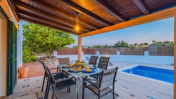 Patio esterno con piscina, tavolo da pranzo, sedie e vista sul paesaggio circostante.