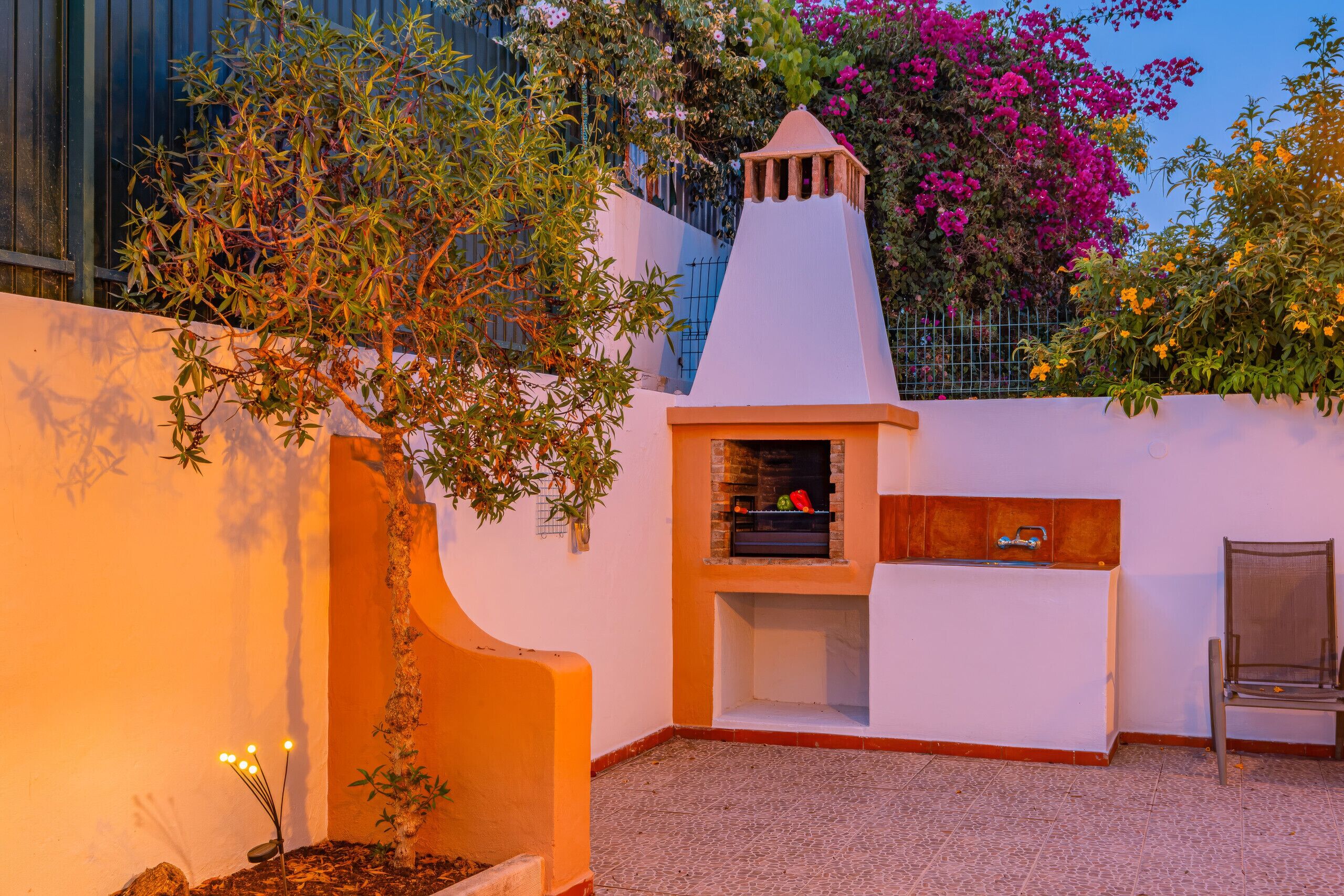 An outdoor patio area with a brick oven, a chair, and a small tree.