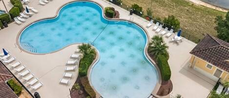 Ein großer, nierenförmiger Pool mit Liegestühlen und Sonnenschirmen, umgeben von gepflegter Bepflanzung und Blick aufs Meer.