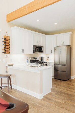A modern kitchen with white cabinetry, a central island, stainless steel appliances, and a wooden ceiling beam. - Luxury Retreat for Discerning Couples and Business Travelers (Vermilion)