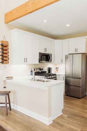 A kitchen with white cabinets, a stainless steel refrigerator, a built-in oven, and a wooden ceiling beam. - Luxury Retreat for Discerning Couples and Business Travelers (Vermilion)