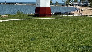 Un faro con base bianca e rossa, posto su una zona erbosa vicino a una spiaggia sotto un cielo azzurro.
