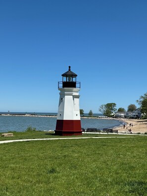 A lighthouse with a white and red base, situated on a grassy area near a beach with a clear blue sky. - Luxury Retreat for Discerning Couples and Business Travelers (Vermilion)