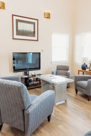 A living room with a flat-screen TV, grey upholstered chairs, a glass-top coffee table, and a framed picture on the wall. - Luxury Retreat for Discerning Couples and Business Travelers (Vermilion)