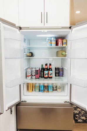 An open refrigerator with multiple shelves containing various beverages and a bottle of champagne. - Luxury Retreat for Discerning Couples and Business Travelers (Vermilion)