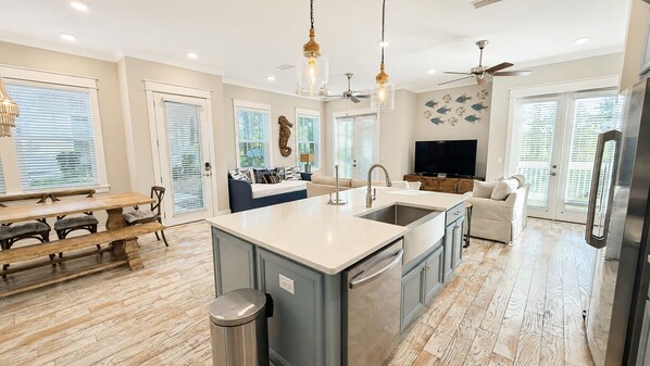 A modern kitchen with a central island, a dining area with benches, and a living space with a sofa and TV.