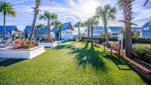 A resort with a well-maintained lawn, palm trees, and a row of blue-roofed buildings. - Stay Anchored at 30a (Watersound)