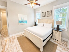 A bedroom with a large bed, a ceiling fan, a nightstand with a lamp, and a window with blinds. - Stay Anchored 30A | 6-Seat LSV + Heated Pool (Watersound)