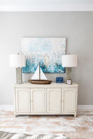 A white cabinet with two lamps, a sailboat model, and a 'STAY anchored' sign. - Stay Anchored 30A | 6-Seat LSV + Heated Pool (Watersound)