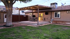 Un jardin avec un patio couvert, un barbecue et des guirlandes lumineuses.