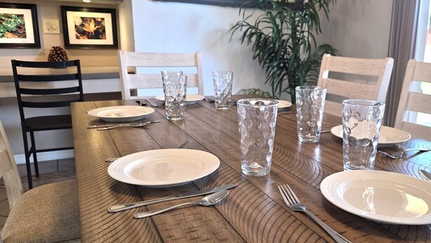 Une table à manger dressée avec des assiettes, des couverts et des verres, entourée de chaises.
