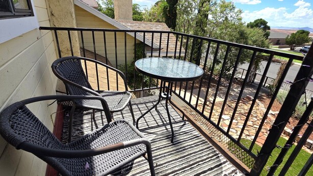 A balcony with two wicker chairs and a small table, surrounded by a black metal railing.