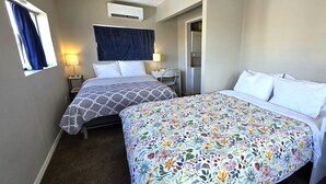 A hotel room with two beds, a desk, a chair, an air conditioning unit, and a window with curtains.