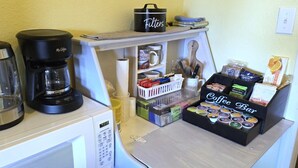 A kitchenette with a coffee maker, a kettle, a microwave, a coffee bar, and various coffee pods.