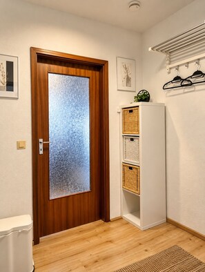 A room with a wooden door, a white cabinet with baskets, a white toilet, and a wall-mounted drying rack. - "Waldblick" Vacation Rental with a Balcony and Rooftop Terrace Offering a Stunning South-Facing View - My SWH (Schonach im Schwarzwald)