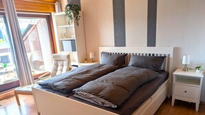 Ein ordentlich bezogenes Bett mit Kopfteil, ein Nachttisch mit Lampe und ein Sessel.