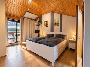 Et soveværelse med træloft, seng med gråt sengetøj, et natbord med lampe og udsigt til en balkon.