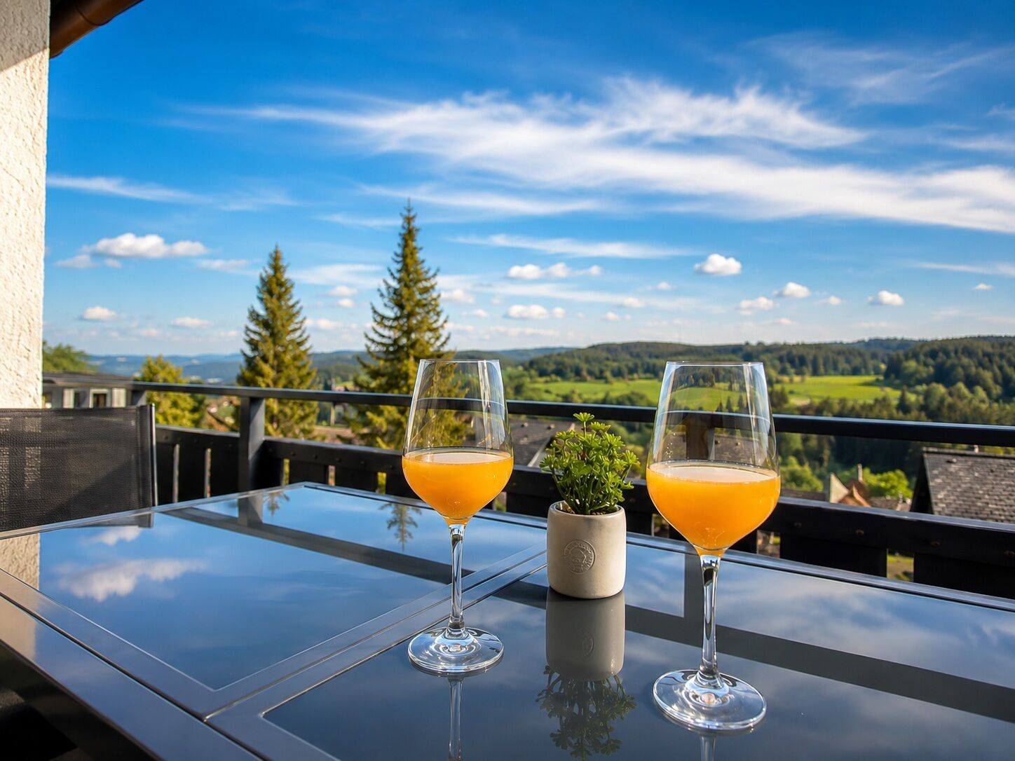 Two glasses of orange juice on a glass table with a view of a mountainous landscape.