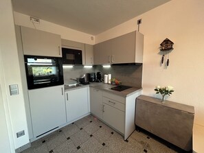 Een kleine keuken met een magnetron, fornuis, spoelbak en een klok aan de muur.