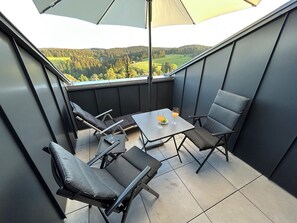 Een balkon met een tafel, stoelen en uitzicht op een bebost landschap.