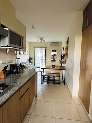 A modern kitchen with a central island, a dining area with a wooden table and chairs, and a built-in microwave above the island. - Apartment in a gated community near the airport - Lirios A13-6 (Cancún)