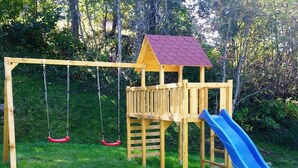 Un parque infantil de madera con columpios y un tobogán.