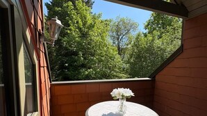 Un balcón con una mesa redonda y sillas, una planta en maceta y vistas a árboles.