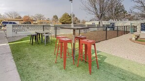 An outdoor seating area with tables and stools, a fenced play area, and a street view. - ⟫ Dog Run & Courtyard 2 Bedroom Apt w/King Bed W&D (Albuquerque)