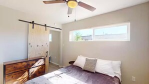 Un dormitorio con una cama, ventilador de techo, ventana y cómoda de madera.