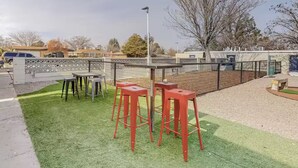 Un espacio exterior cercado con césped artificial, taburetes rojos y una farola.